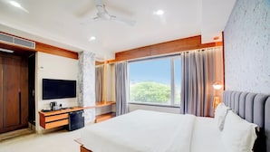 Un dormitorio con una cama, televisión, escritorio, ventana y ventilador de techo.