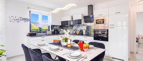 A modern kitchen with white cabinets, a built-in oven, and a dining area with a table set for four.