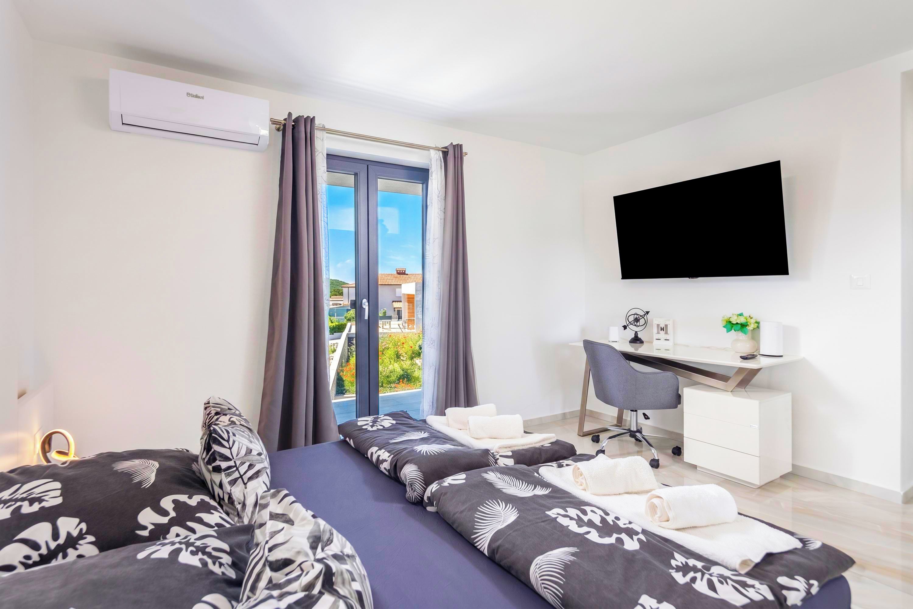A hotel room with a bed, a desk, a chair, a TV, and a view of the outdoors.