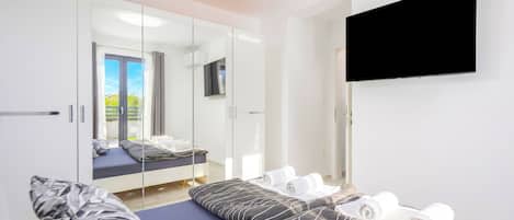 Ein modernes Hotelzimmer mit Bett, Fernseher, Spiegel und Blick ins Freie.