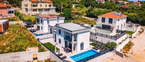A modern two-story house with a swimming pool, large windows, and a balcony.