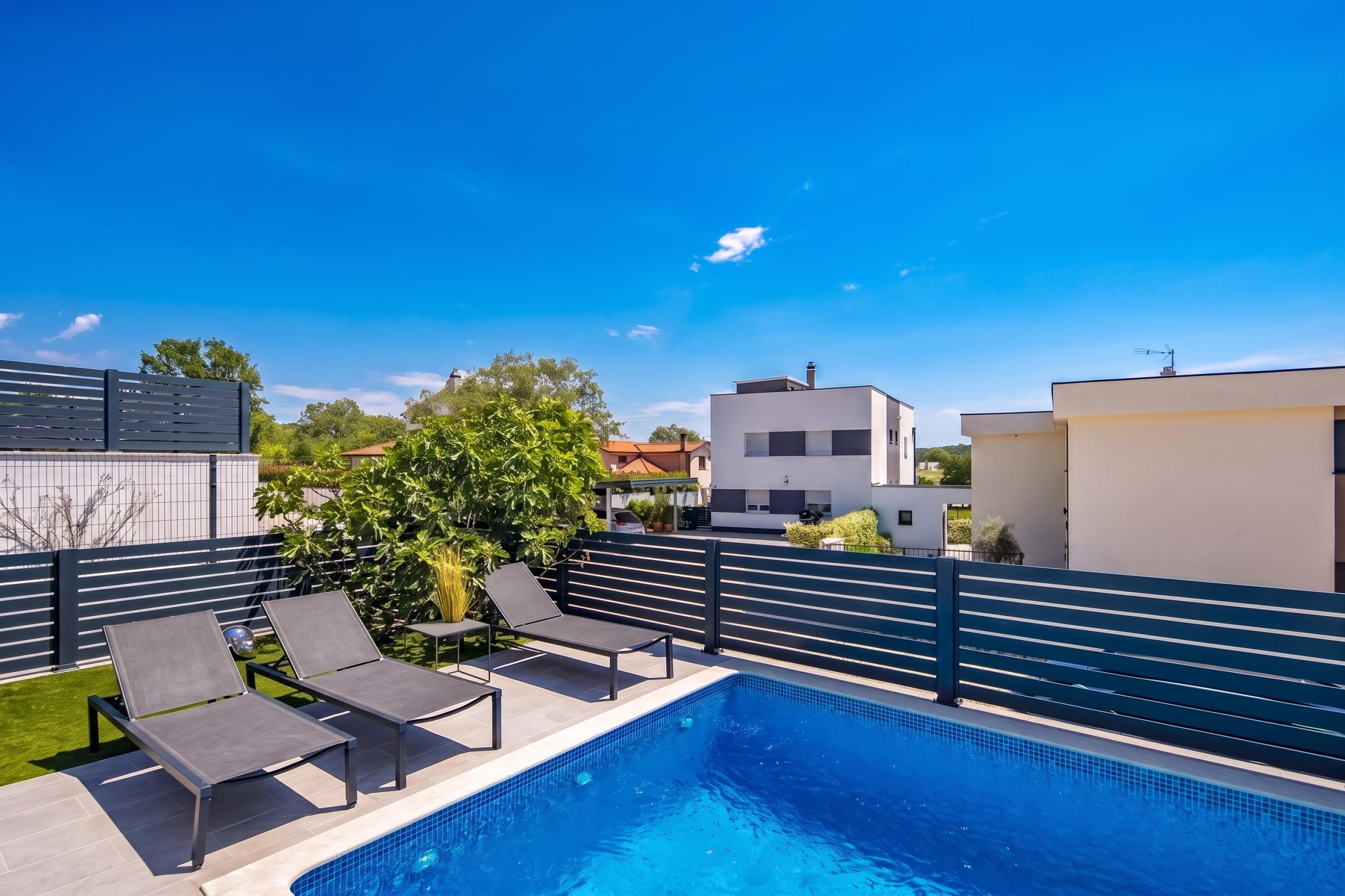 Una piscina con sillas de descanso, una cerca y edificios modernos al fondo.