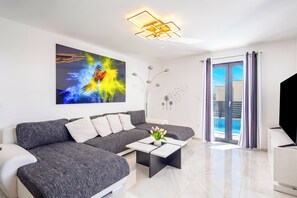 Ein modernes Wohnzimmer mit einem Ecksofa, einem Couchtisch, einem Gemälde, einer Zierpflanze und Blick auf einen Pool durch die Glastür.