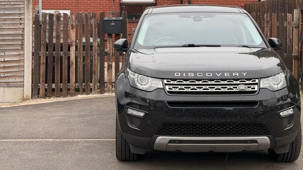 A black Land Rover Discovery parked in front of a wooden fence with a brick building in the background. - Leeds Tranquil Retreat With 3 Bedrooms (Leeds)