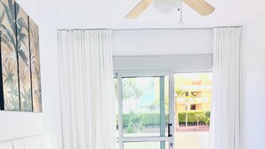 Une chambre d’hôtel avec un lit, une commode en bois, un ventilateur de plafond et une vue sur l’extérieur.