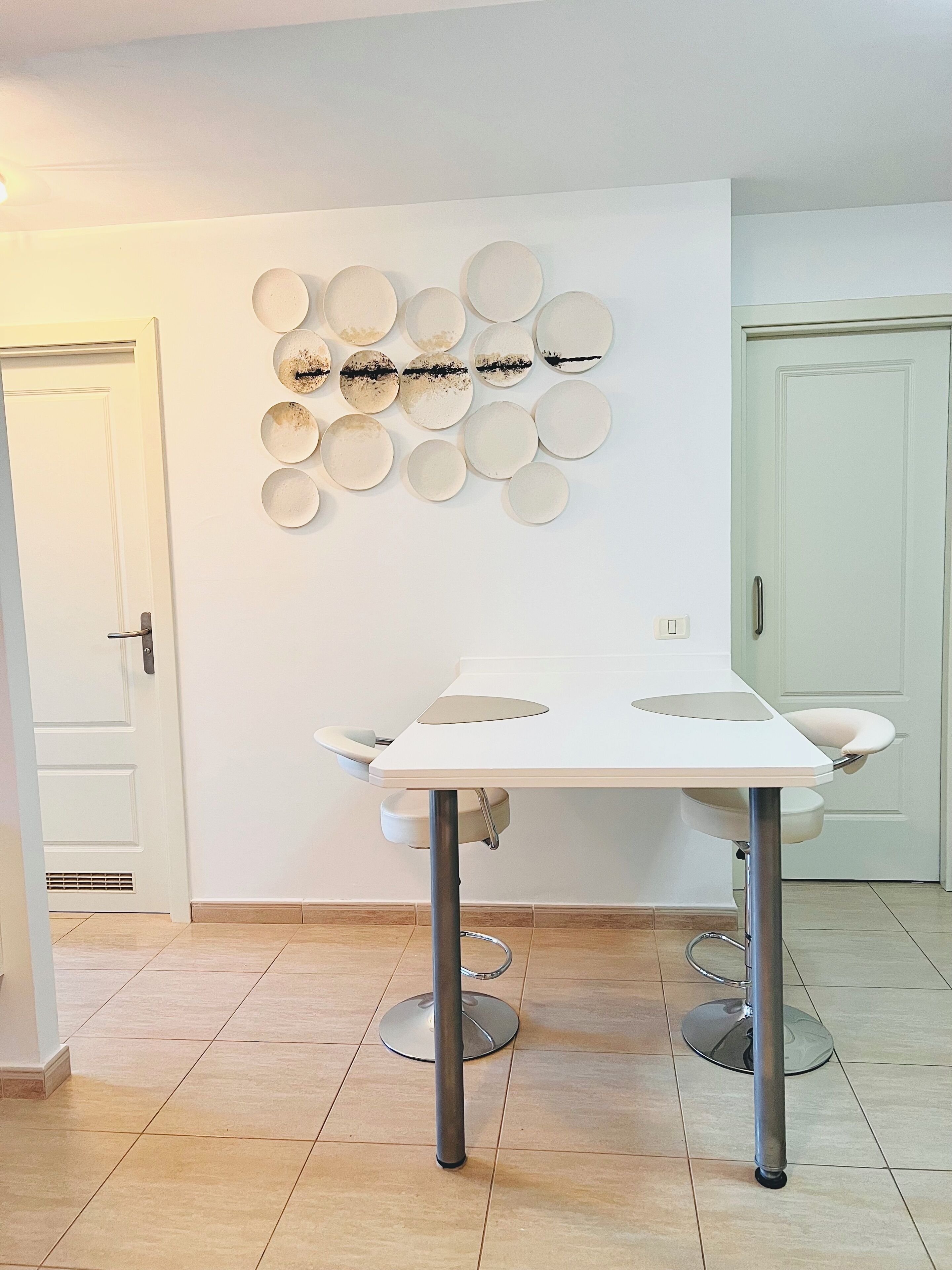 Une pièce avec une table blanche, une décoration murale en forme d’assiette et une porte.