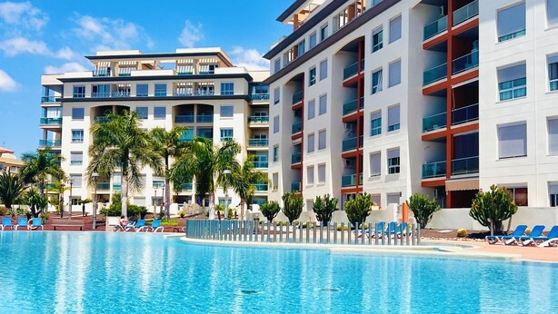 Un hôtel moderne doté d’une piscine, de nombreux balcons et offrant une vue sur un ciel d’un bleu éclatant.