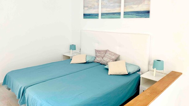 Slaapkamer met een bed, twee nachtkastjes, een hanglamp en een wand met drie schilderijen.