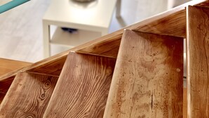 Een houten trap leidt naar een woonkamer met een witte salontafel en een bank.