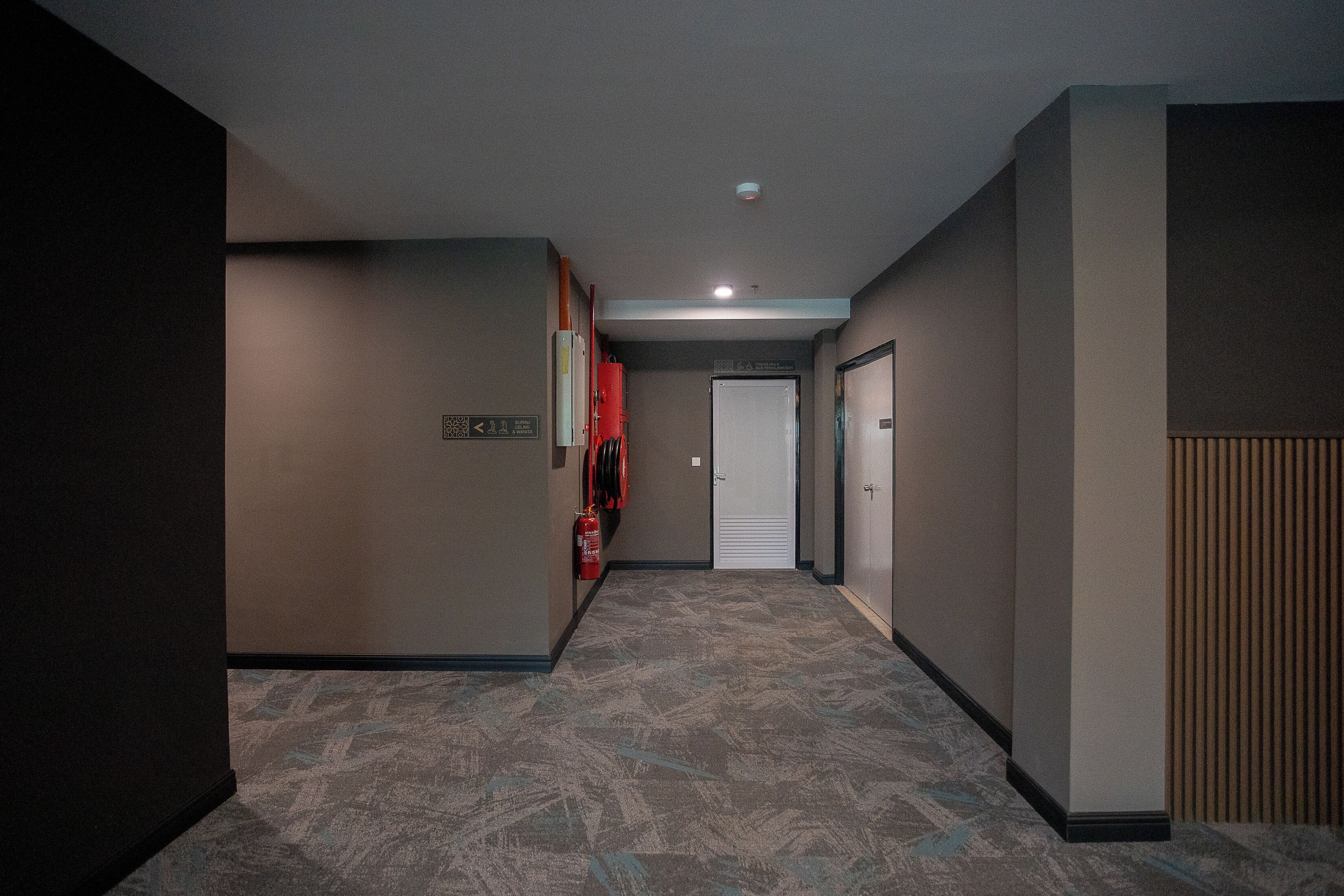 Un pasillo con piso alfombrado, un extintor y una puerta al final.