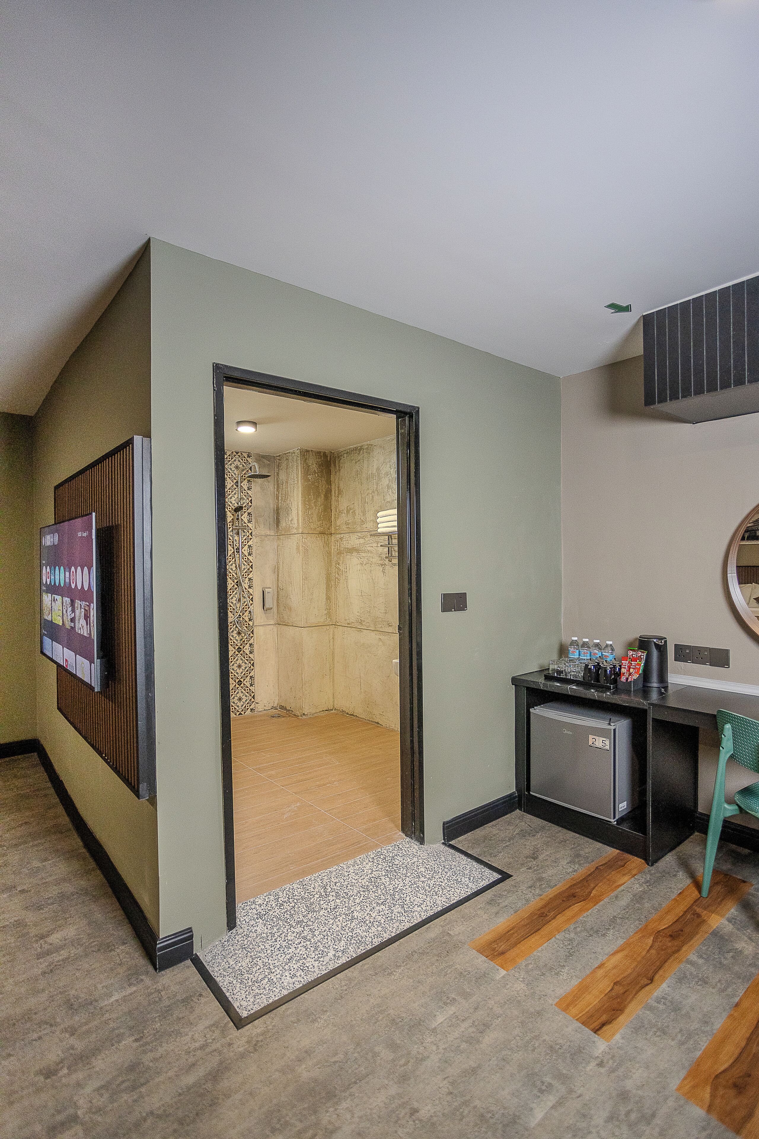 Habitación de hotel con ducha, un pequeño escritorio con cafetera, televisión y puerta que da al baño.