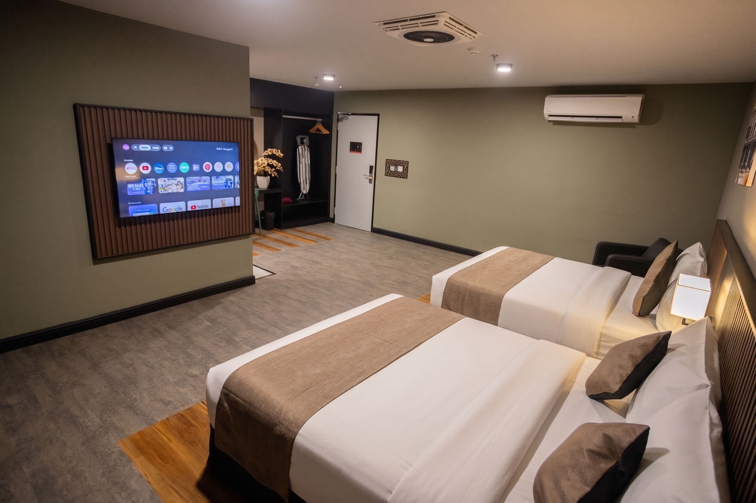 Quarto de hotel com duas camas, uma televisão fixada na parede e um ar condicionado.