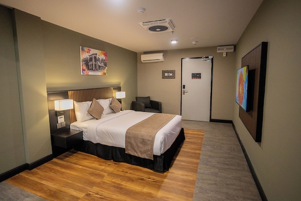 Habitación de hotel con cama, lámparas de noche, mesita de noche, una puerta y un equipo de aire acondicionado en la pared.