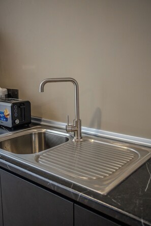 Una cocina con un lavamanos de acero inoxidable, un tostador y un grifo empotrado en la pared.