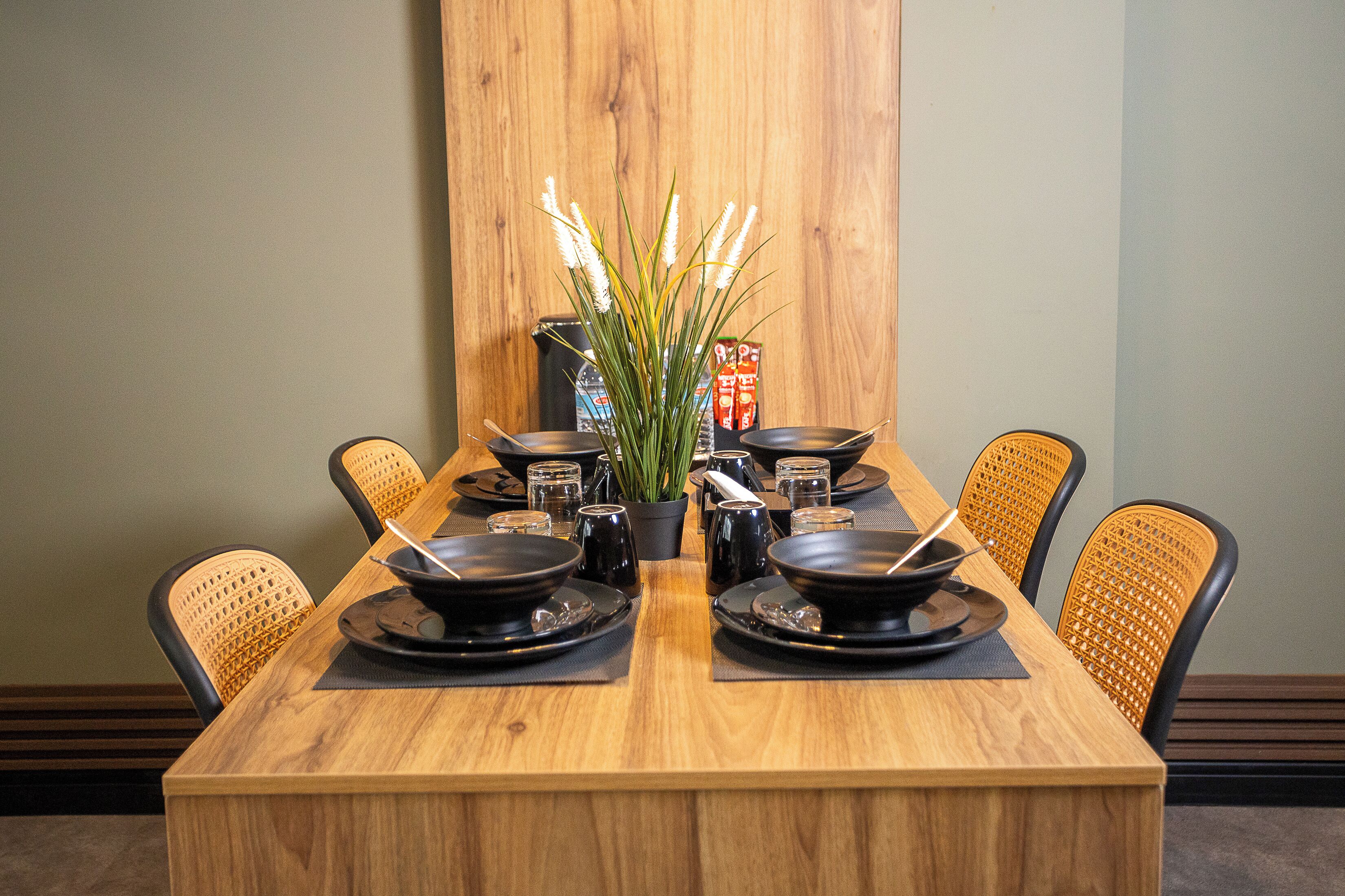 A wooden dining table set for six with black plates, bowls, and chopsticks.