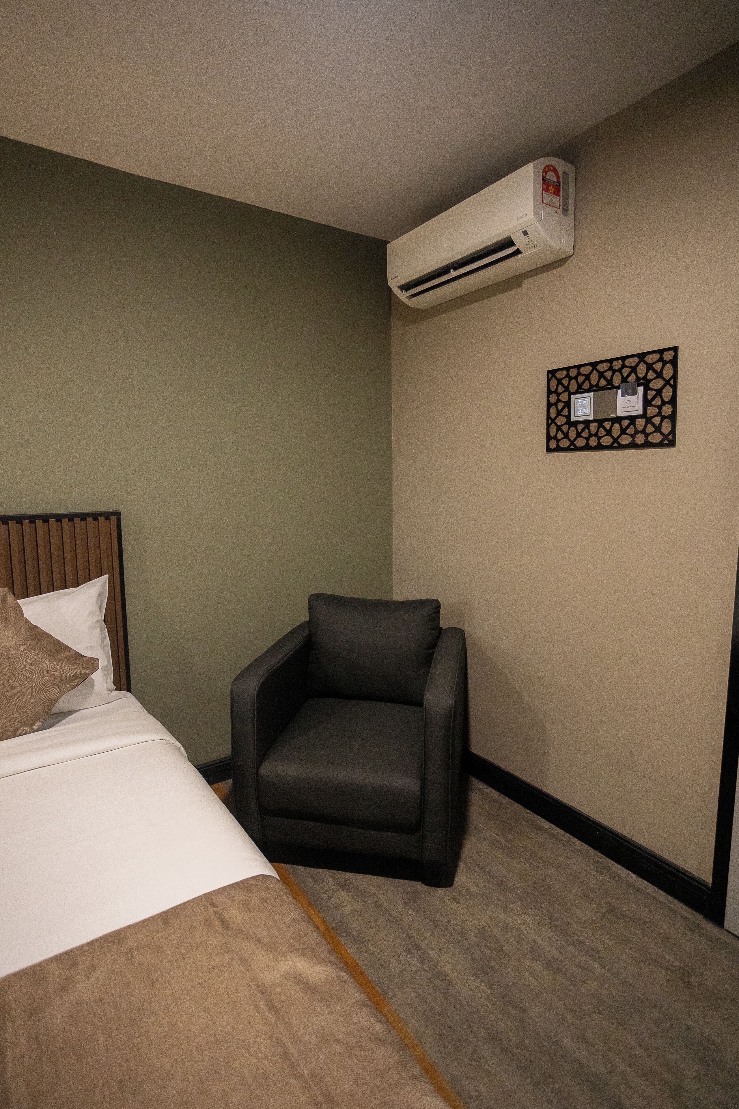 Une chambre d’hôtel équipée d’un lit, d’une chaise, d’un climatiseur et d’un panneau de commande fixé au mur.