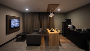 A modern living room with a flat-screen TV, a wooden coffee table, a sofa, and a kitchen area with a refrigerator and a sink. - HOTEL VALYA MELAKA SENTRAL RIVERFRONT (Malacca City)