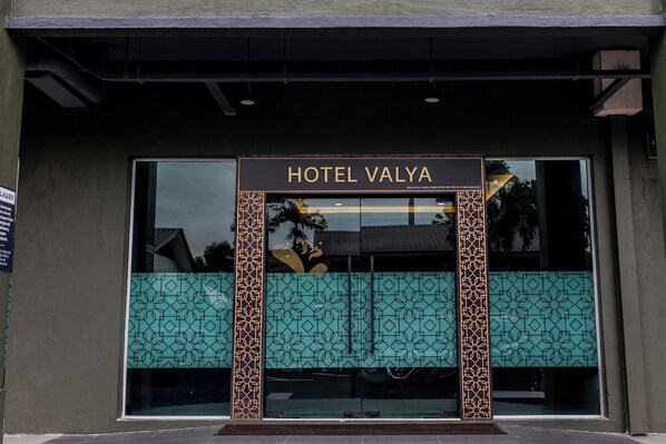 La entrada del Hotel Valya, con un amplio ventanal de vidrio, un letrero encima de la entrada y paneles decorativos a cada lado.