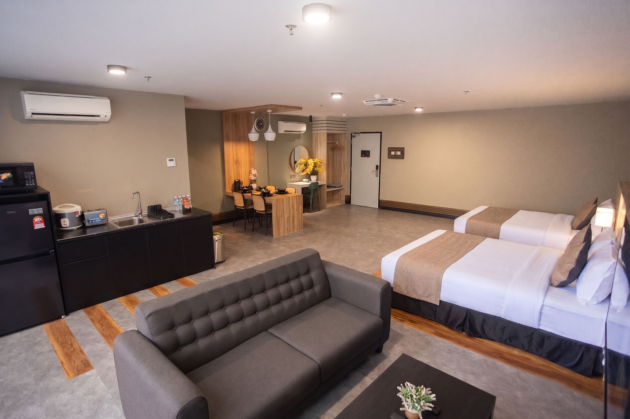 Habitación de hotel con sofá, cama con edredón, una mesita, microondas, hervidor y lavabo.