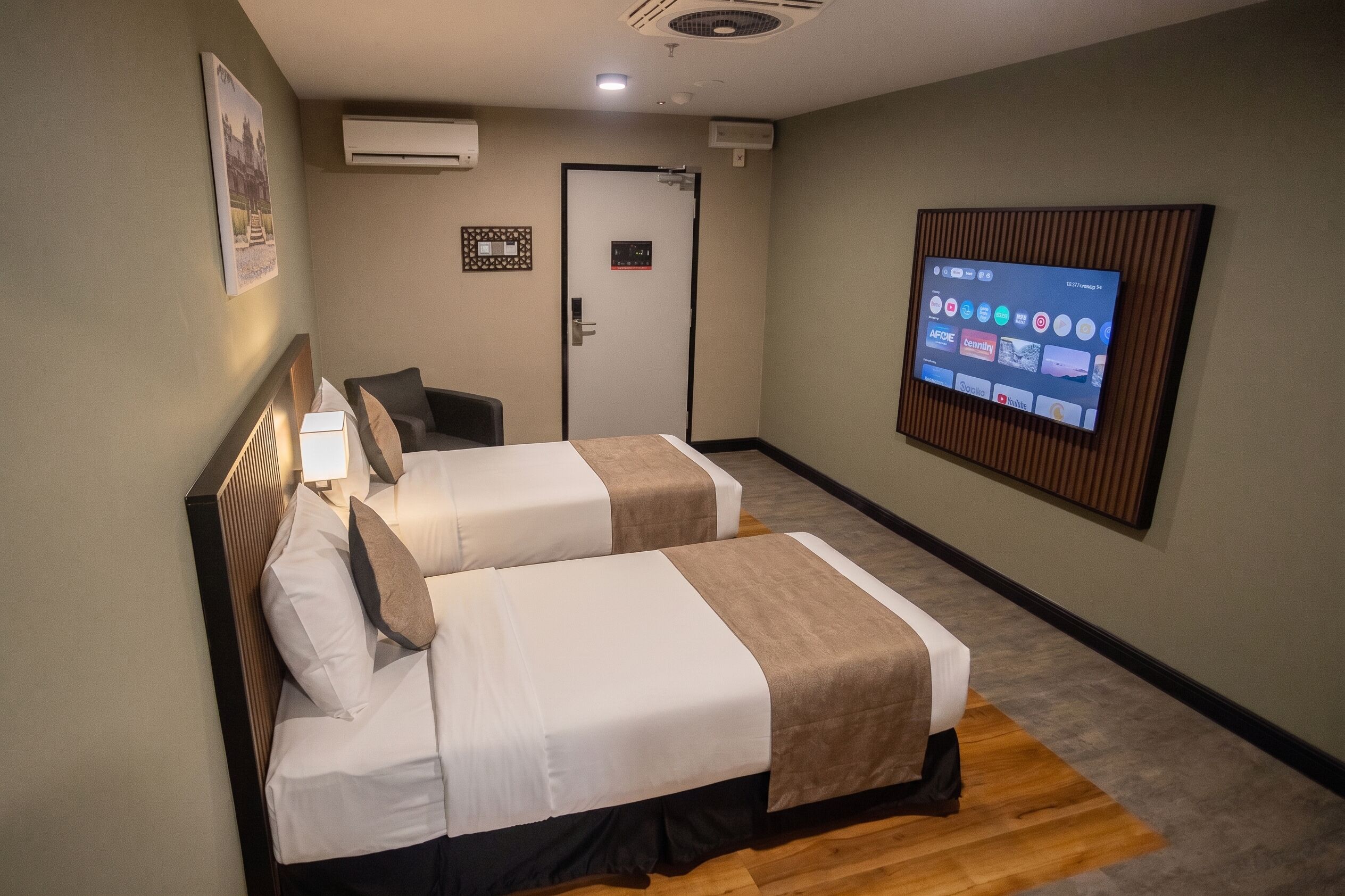 A hotel room with two beds, a television mounted on the wall, and an air conditioning unit.