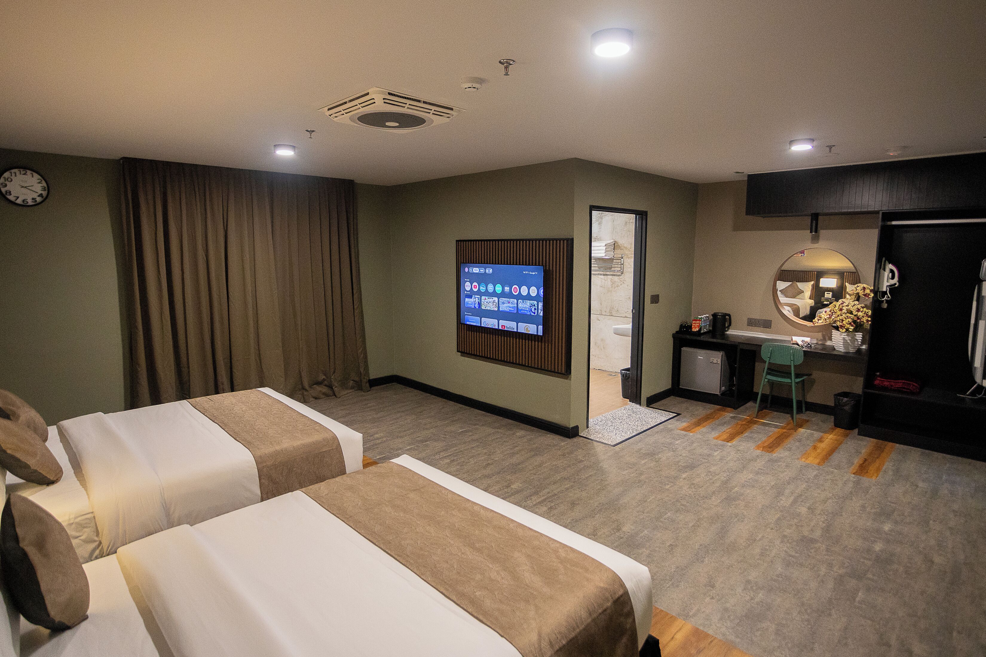 Habitación de hotel con dos camas, un escritorio, televisión y baño visible a través de una puerta abierta.
