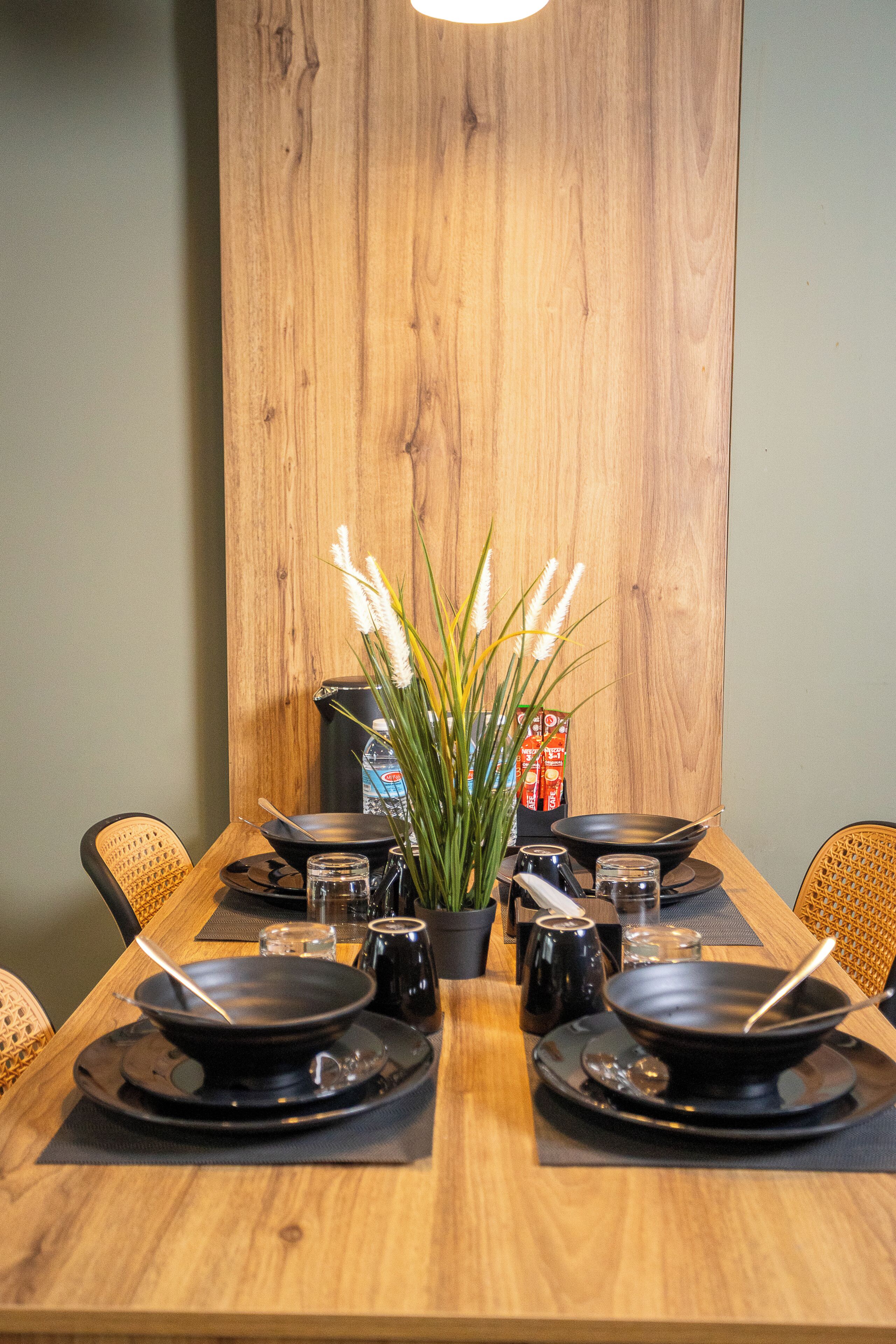Een eettafel gedekt met zwarte borden, kommen en stokjes, met een potplant in het midden.