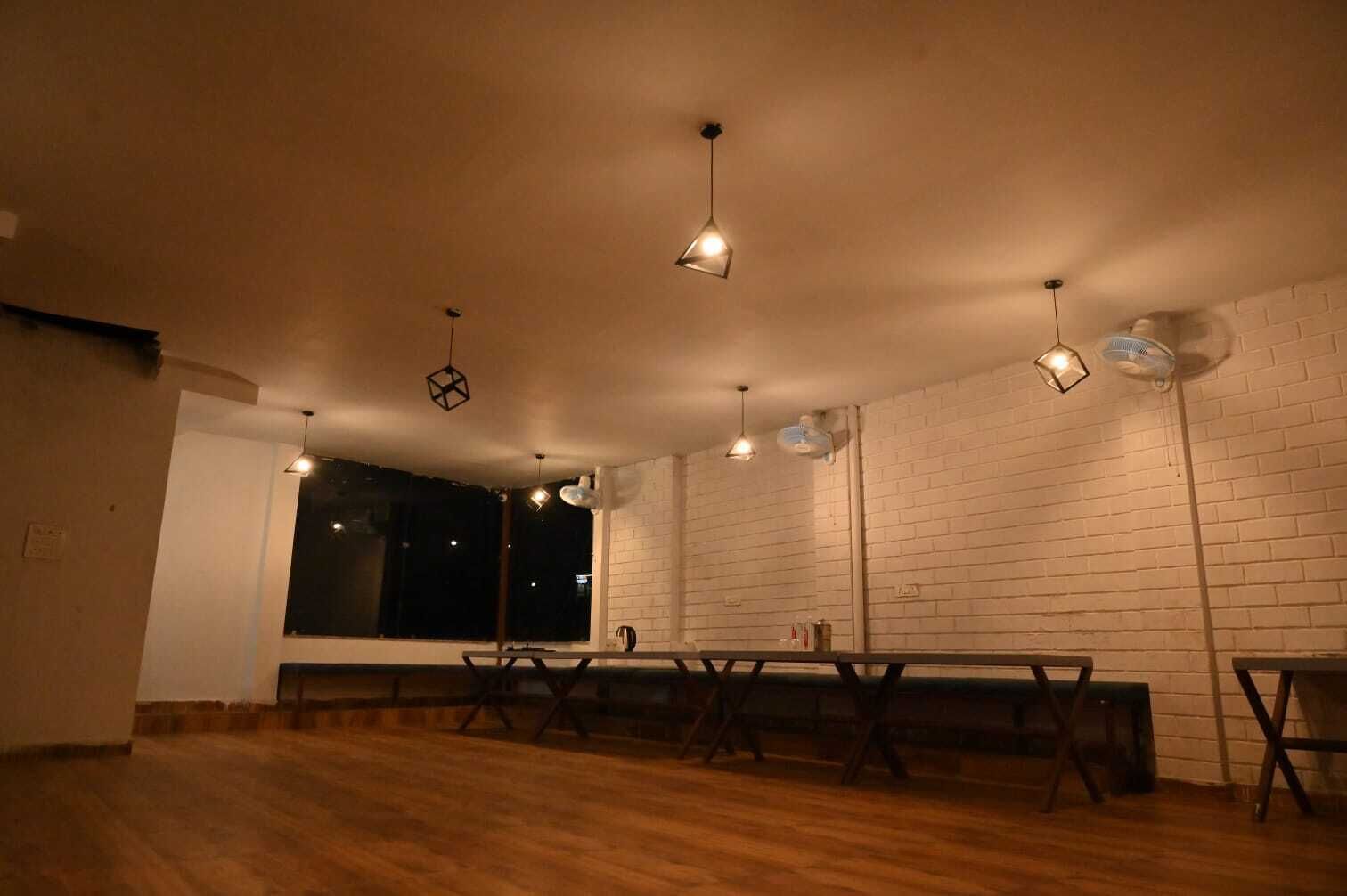 Una habitación con piso de madera, paredes de ladrillo blanco, una mesa larga y lámparas colgantes.