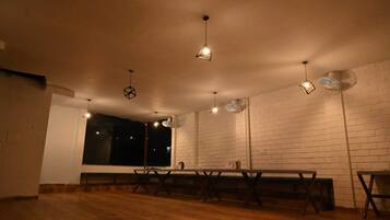 Una habitación con piso de madera, paredes de ladrillo blanco, una mesa larga y lámparas colgantes.