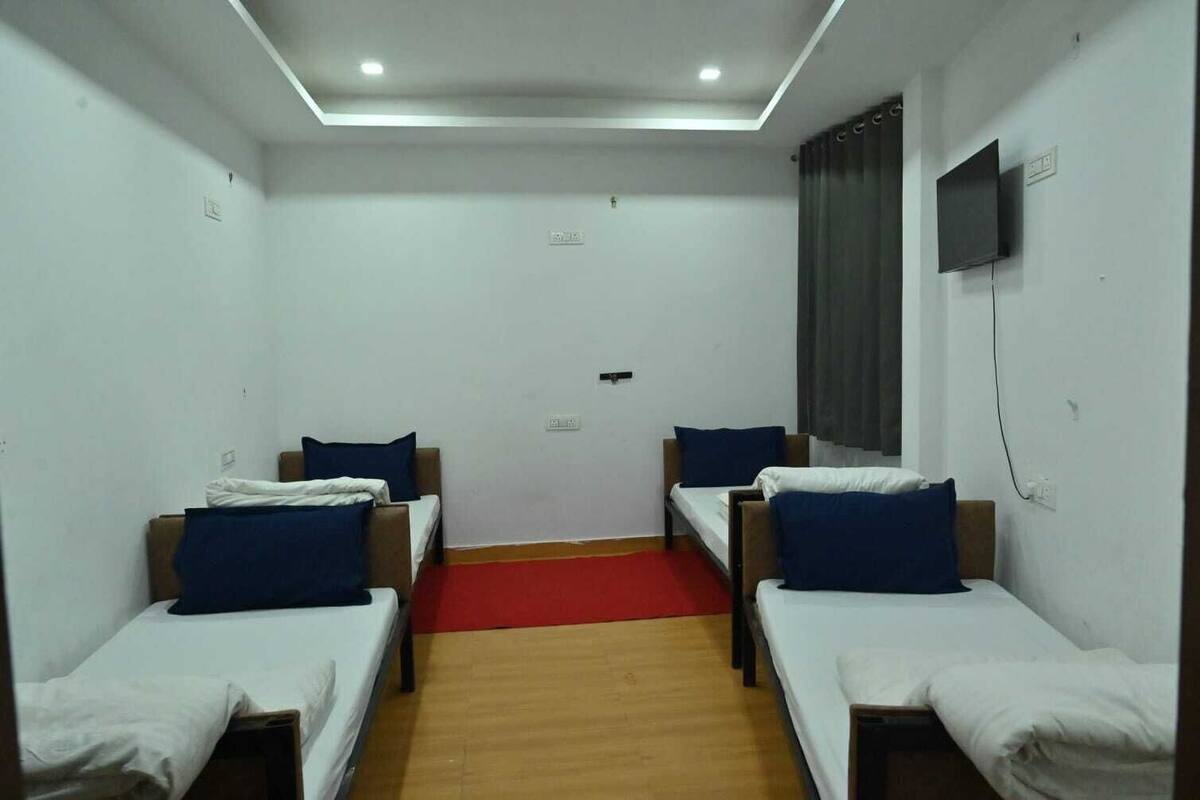 A room with two single beds, a red carpet, a flat-screen TV on the wall, and a wooden floor.