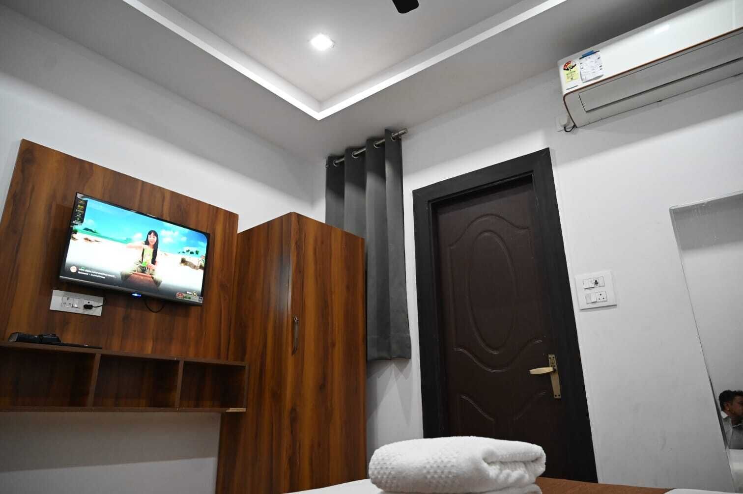 Habitación con televisión montada en un mueble de madera, una puerta oscura y una toalla blanca sobre una mesa.