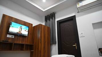 Habitación con televisión montada en un mueble de madera, una puerta oscura y una toalla blanca sobre una mesa.