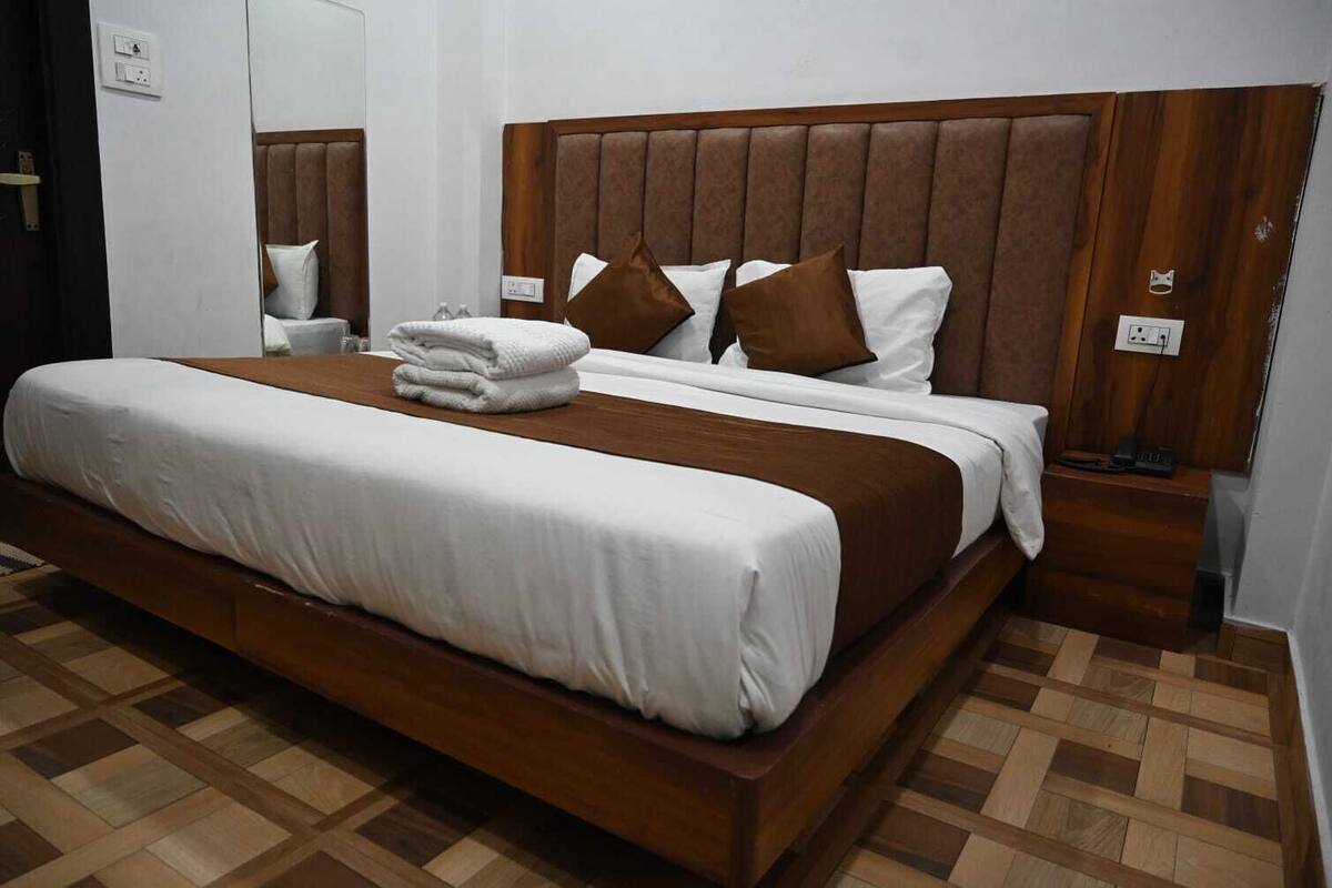A hotel room with a large bed, wooden headboard, and a bedside table with a lamp.
