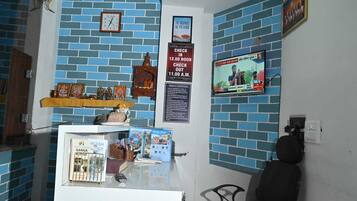 Zona de recepción con un reloj, una televisión y un cartel que indica horarios de registro de entrada y salida.