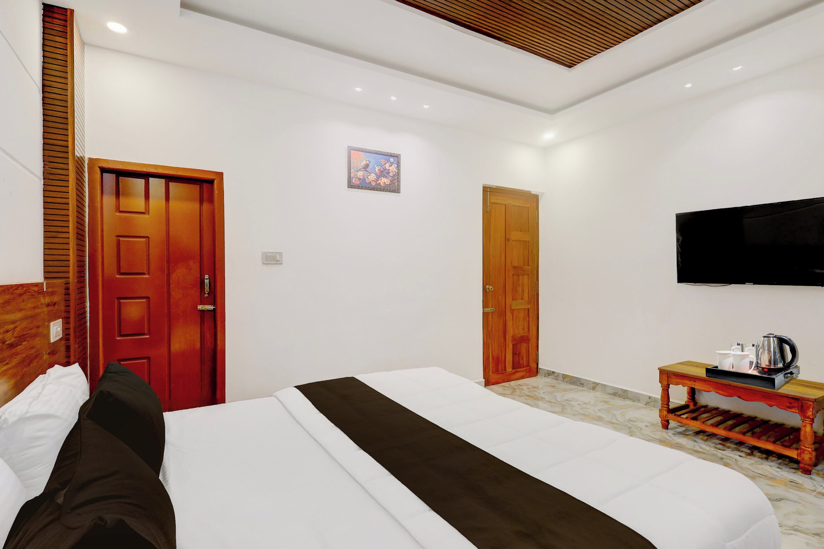 Quarto de hotel com uma cama, televisão, uma pequena mesa de madeira com um chuveiro e duas portas de madeira.