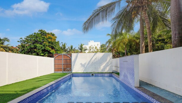 A swimming pool with a tiled edge, surrounded by a white wall and a wooden gate.