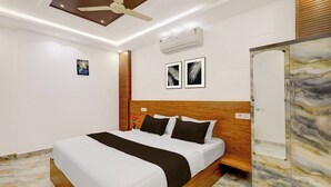 A modern hotel room with a bed, ceiling fan, air conditioning unit, and artwork on the walls.