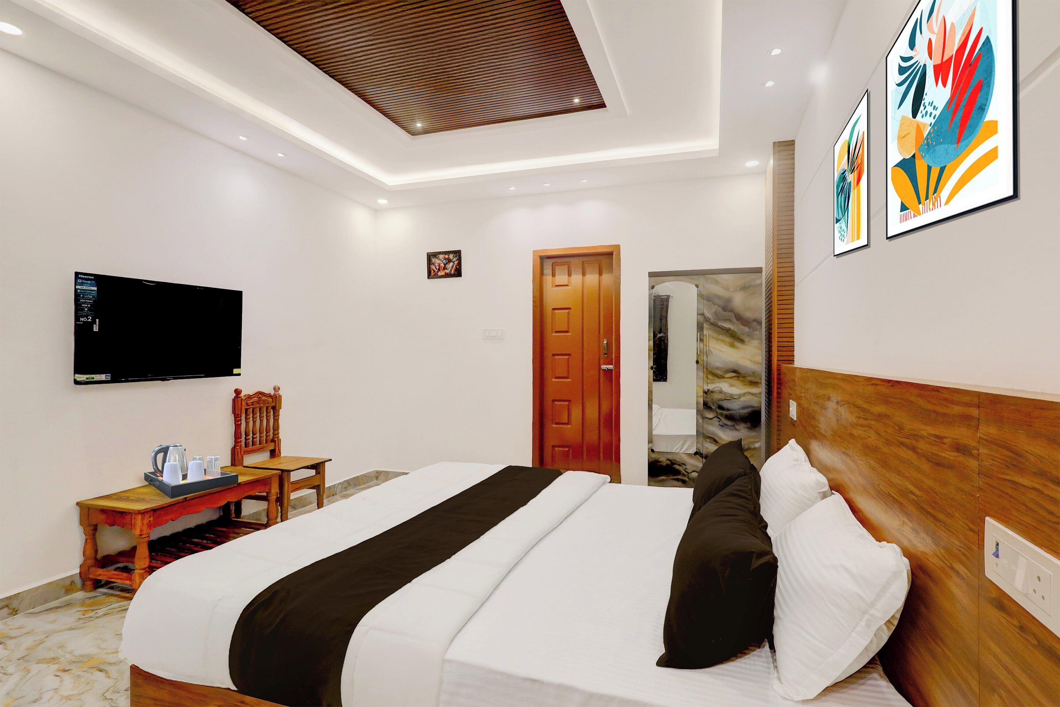 A hotel room with a bed, a television, a desk with a chair, and artwork on the wall.