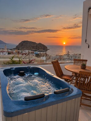 A hot tub with a view of the sunset over the sea, a wooden table, and chairs.