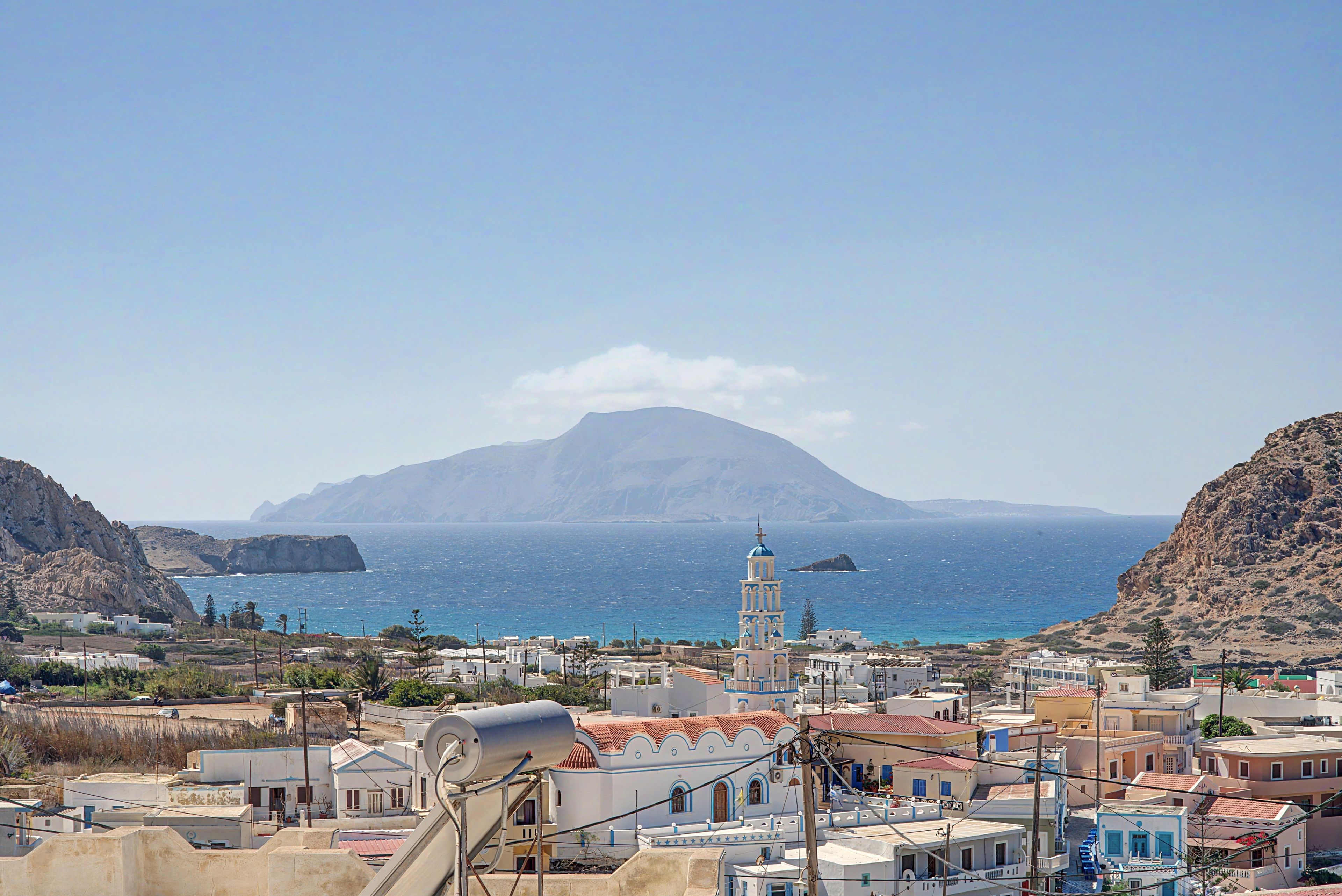 A coastal town with a prominent church tower, rocky cliffs, and a mountain in the background.