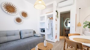 Un salon moderne avec un canapé gris, une table ronde en bois et une table à manger blanche avec des chaises. On y trouve des assiettes décoratives fixées au mur et un luminaire suspendu.