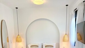 Une chambre moderne avec un grand lit, deux lampes de chevet, un miroir rond et un téléviseur.