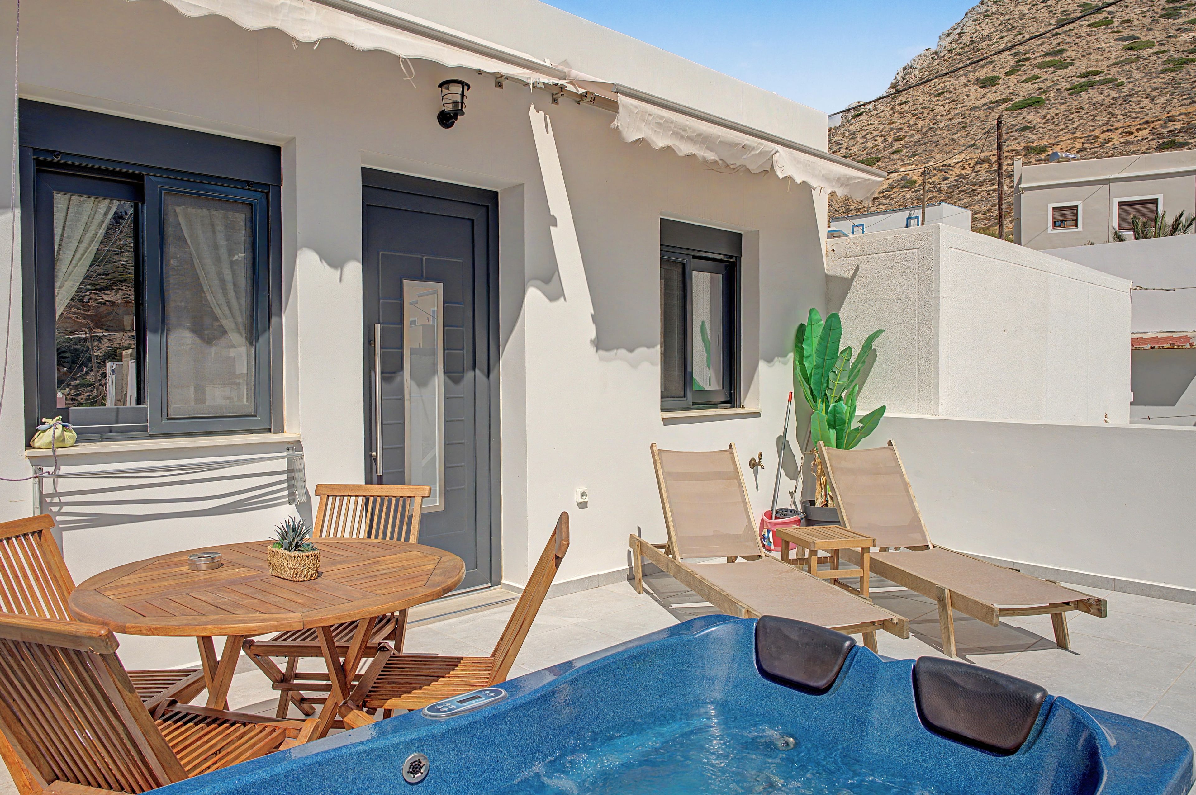 A poolside area with a wooden table and chairs, a hot tub, and a potted plant.