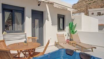 A poolside area with a wooden table and chairs, a hot tub, and a potted plant.