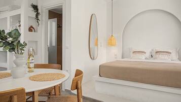 A modern bedroom with a bed, bedside table, and a dining area with chairs and a table.