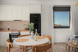 A modern kitchen with white cabinets, a black refrigerator, and a dining area with a round table and wooden chairs. - Majestic View Villa Studio with Sea View and Jacuzzi (Arkasa)