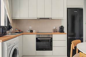 A compact kitchen with a washing machine, oven, refrigerator, and a coffee maker on the countertop. - Majestic View Villa Studio with Sea View and Jacuzzi (Arkasa)