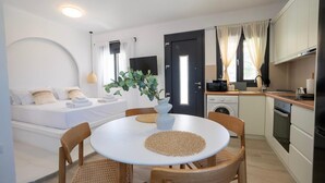 Une chambre moderne comprenant un lit, une table à manger avec des chaises, un coin cuisine et une grande fenêtre avec des rideaux.