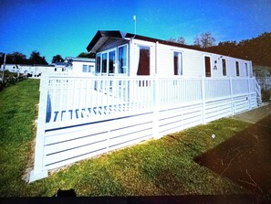 Une maison mobile blanche, dotée d’une véranda clôturée, d’un petit garage attenant et surplombée par un ciel dégagé.