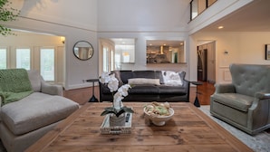 A spacious living room with a wooden coffee table, a sofa, and a chair. - Welcome to this spectacular home, which stands out for its soaring stone fireplace, a bright sunroom, and a unique indoor-outdoor entertainment lounge with a classic arcade game! (Elliston)