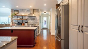 A modern kitchen with a central island, built-in appliances, and a hallway leading to a door. - Welcome to this spectacular home, which stands out for its soaring stone fireplace, a bright sunroom, and a unique indoor-outdoor entertainment lounge with a classic arcade game! (Elliston)